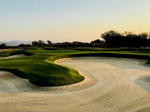 a sand trap with a green grass and trees in the background