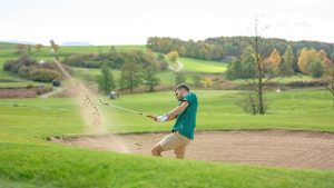 a man hitting a golf ball with a golf club out of the bunker
