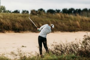 a man swinging a golf club out of the bunker and rough