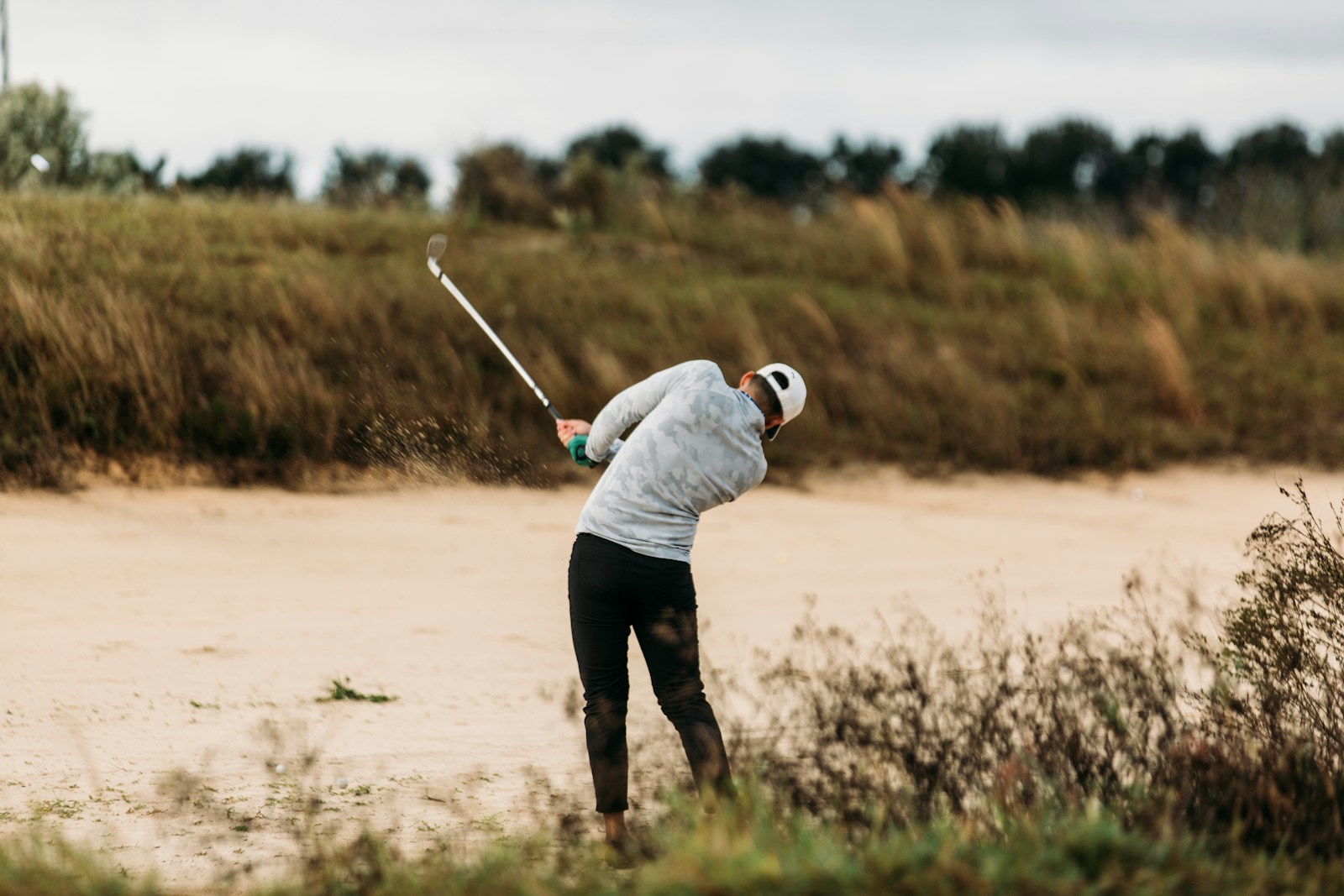 a man swinging a golf club out of the bunker and rough